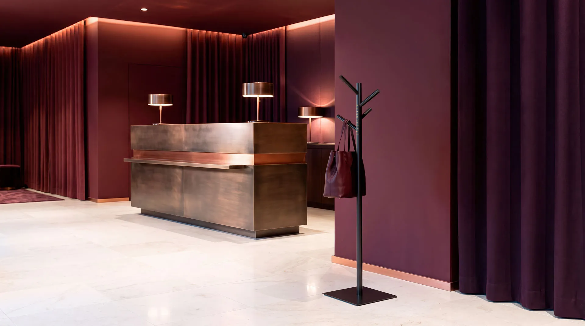 Taschenbaum stehend in einer Hotel Lobby und trägt an einem der Äste eine Tasche. Das bild ist im Farbstil violett, warm Gold und weiss. Ein Stilbild das in ein Interior-Design Magazin passen würde.